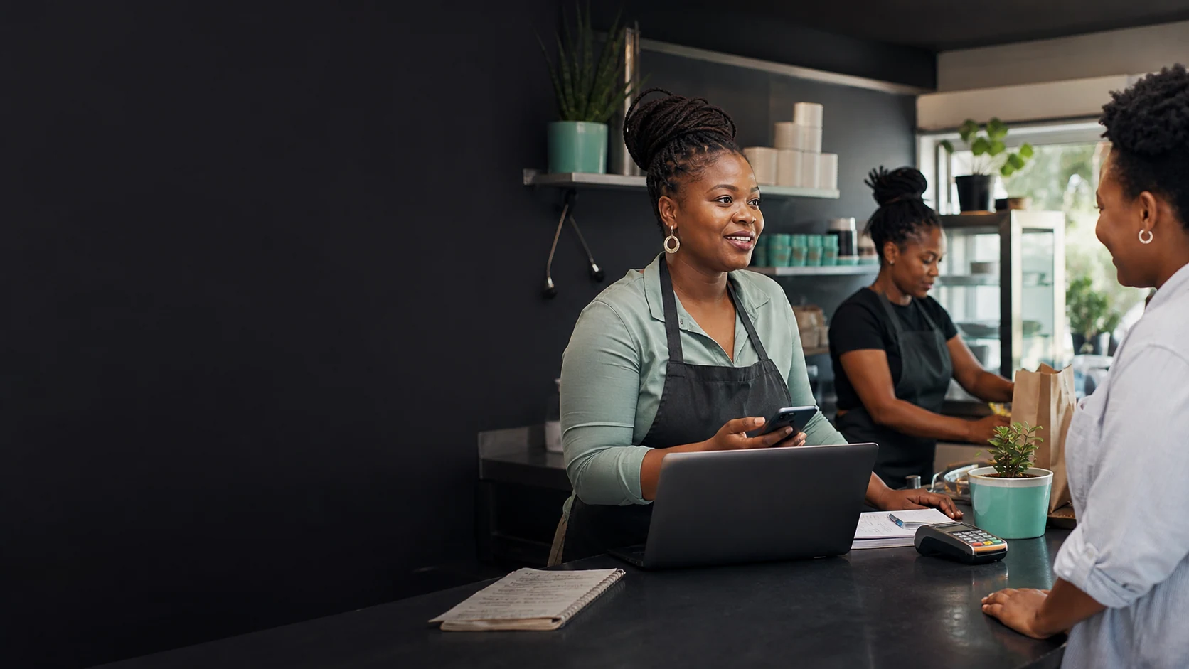 A South African small-business owner helping a customer while using a phone and laptop